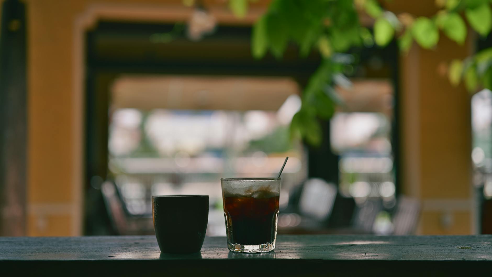 Coffee mug and iced drink on a balcony table in a tranquil setting.